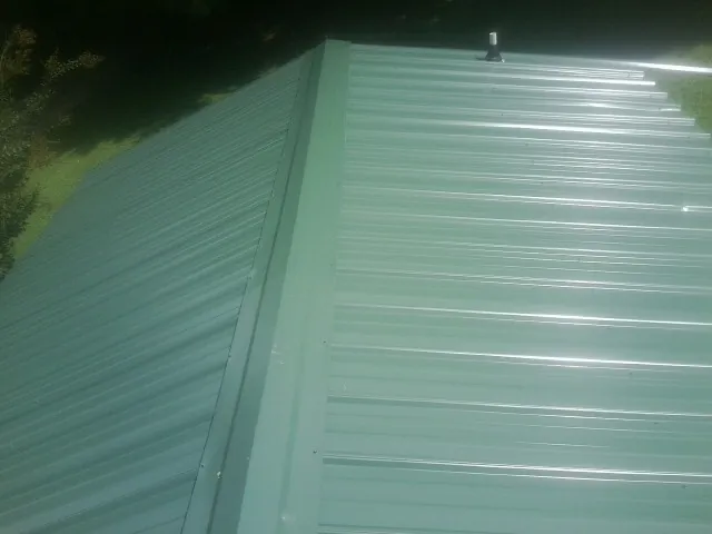 New green metal panels meeting at the ridge of a roof — Flat Roof Repair work by our crew in Imbler