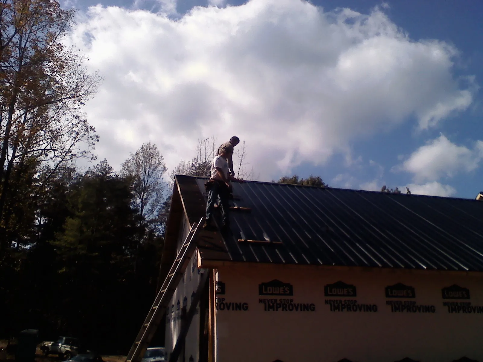 Roofer fastening dark metal panels high against a cloudy sky, from a Roof Inspection job in Imbler